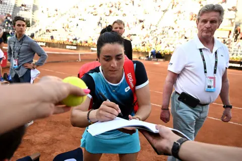 Reuters May 13, 2022 Tunisia"s Ons Jabeur signs autographs for fans after winning her quarter final match against Greece"s Maria Sakkari