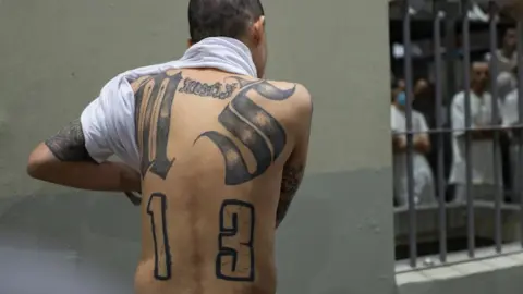 Lissette Lemus/BBC A prisoner shows his back tattooed with symbols of the Mara Salvatrucha gang