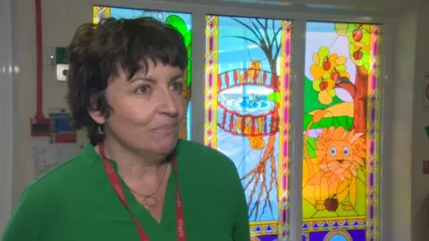 Deputy head Nia Jones standing in front a a stained glass window at the school which depicts a cartoon lion and other characters