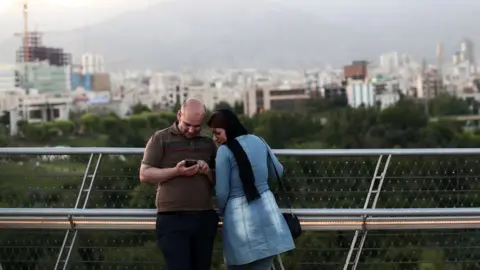 AFP/Getty Images An Iranian couple look at pictures on their smartphone on the 'Nature' bridge in the capital Tehran on 2017