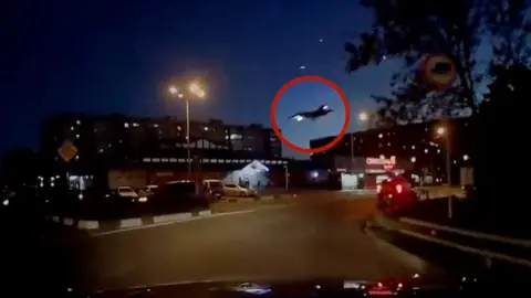 Still from dashcam footage: plane about to crash into buildings