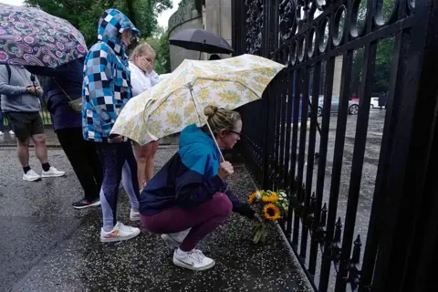 Jane Barlow/PA A member of the public lays flowers at the gates of the Palace of Holyroodhouse in Edinburgh