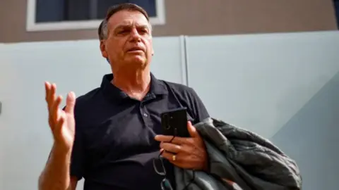 Jair Bolsonaro gestures while standing in front of his house before testifying to the Federal Police in Brasilia, Brazil, last month