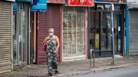 Getty Images A woman walking along Cardiff street with closed shops behind