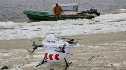 Drone Delivery Canada Drone sits on beach if front of a speed boat