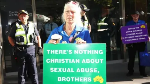 Getty Images A protester outside a court hearing for Pell holds a sign saying: "There's nothing Christian about sexual abuse, brothers."