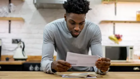 Getty Images Man in kitchen looking at paper bill