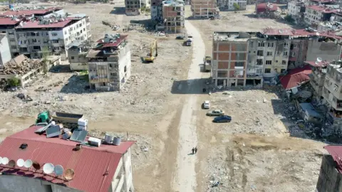 Goktay Koraltan/BBC A photo from a drone showing just a few buildings standing among empty space after rubble has been cleared away