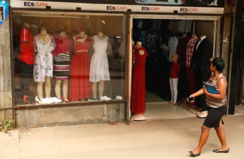 Reuters A woman walks past a shop front in Harare, Zimbabwe. It has a sign above the windows and doors bearing the EcoCash logo, to tell passersby that it accepts that form of payment. Tuesday 20 February 2019