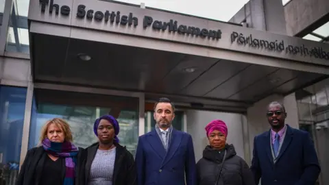 Getty Images Debrah Cole, the director of Inquest, and lawyer Aamer Anwar with the Bayoh family outside the Scottish Parliament