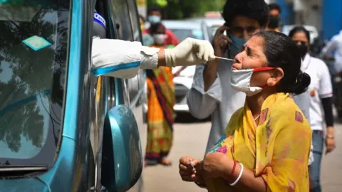 Getty Images A health worker of Special Mobile Surveillance team in PPE coveralls collects a swab sample from a woman for Covid-19 rapid antigen test, at Model Town, on July 15, 2020 in New Delhi, India