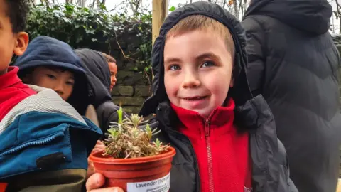 Pete Hughes Image of a boy holding a small lavender plant.