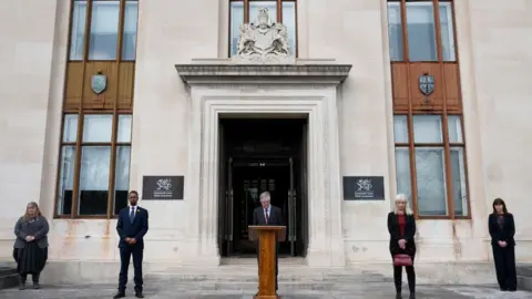 Getty Images First Minister of Wales Mark Drakeford (centre) takes part in a minutes silence on the steps of the Welsh Government Building in Cathays Park with Julie James MS (far left), Vaughan Gething MS (2nd left) Dame Shan Morgan (fourth from left) and Lesley Griffiths MS (right) on March 23, 2021 in Cardiff, United Kingdom