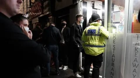 PA Media A police officer reminds workers in Newcastle city centre of the 10pm curfew that pubs and restaurants in England are subject to in order to combat the rise in coronavirus cases.