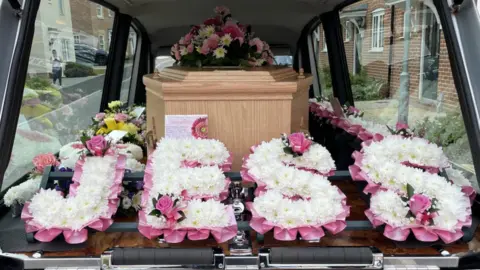 Stout Family Jessica Mai Walden's coffin in the funeral car with flowers that spell out Jess