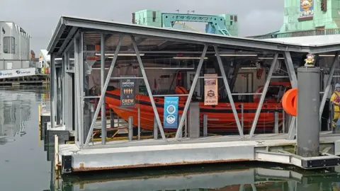 A glass-sided lifeboat house containing the orange inshore lifeboat at Poole Lifeboat Station