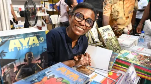 Issouf Sanogo/ AFP Ivorian writer Marguerithe Abouet, author of comic book "Aya de Yopougon" poses for a photo during the Abidjan International Book fair in Abidjan on May 13, 2023.