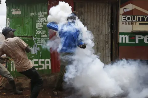 DAI KUROKAWA/ EPA A supporter of the opposition coalition the National Super Alliance is covered by a cloud of tear gas as he throws a canister back at police officers
