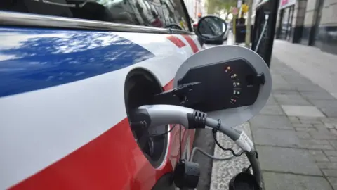 JEFF OVERS Electric Mini Cooper car charging on a street side charging point in Westminster, London