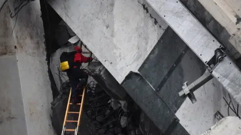 EPA A rescuer climbs a ladder up into large slab of road concrete