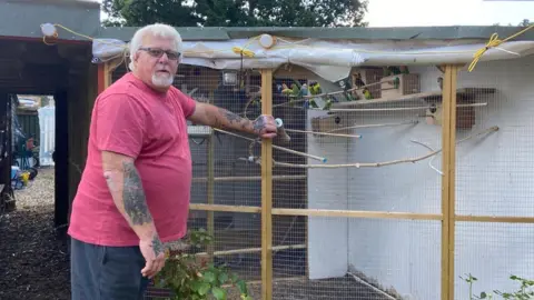 Drew Holdaway a man in a red top stands by an aviary