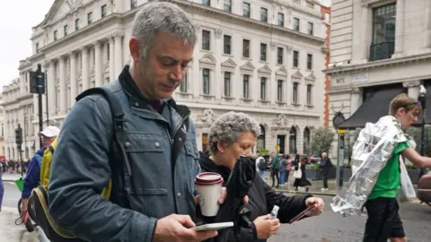 PA Media People looking at their mobile phones on Regent Street in London