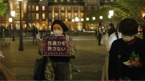 Woman holds placard saying "sexual abuse is unforgiveable" at a Flower Demo in central Tokyo