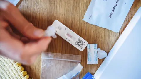 Getty/ Tang Ming Tung A woman squeezing the sample liquid on a test strip while carrying out a Covid-19 rapid self test at home.