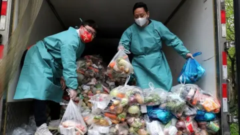 Reuters Workers wearing protective gear sort bags of vegetables and groceries on a truck to distribute them to residents at a residential compound during lockdown in Shanghai on 5 April