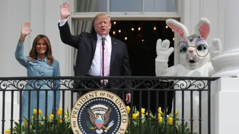 US President Donald Trump and first lady Melania Trump wave beside a person in an Easter Bunny costume on the Truman balcony of the White House