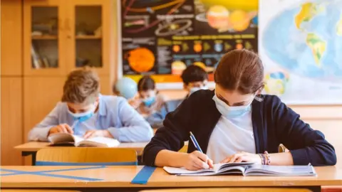 izusek/Getty Images High school students at school, wearing face masks at desks