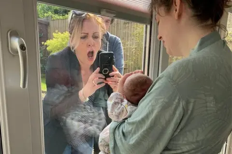 Laura Dally Woman looks overjoyed as she takes picture of baby through a window