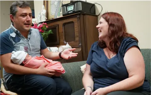 Jesús and Marissa chatting, with the baby in her father's arms