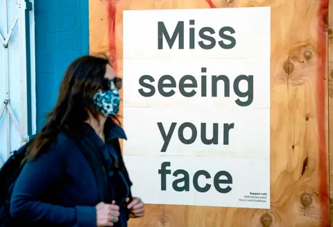 Josh Edelson / AFP A woman in a face mask walks past a sign