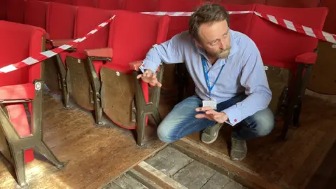 Jill Bennett/BBC A man kneeling inside St George's Guildhall theatre in King's Lynn