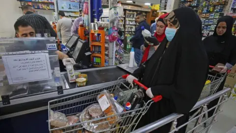 AFP A woman waits at the till of a supermarket in Baghdad before the start of a curfew