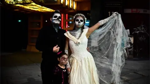 AFP A couple and their daughter show off their costumes during the Catrinas parade.