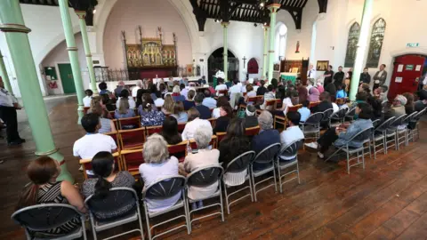 PA People sitting inside St Clement's Church