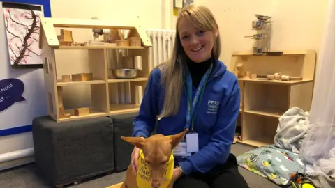 Libby Bowles sitting on a classroom floor with Pip by her side smiling into the camera