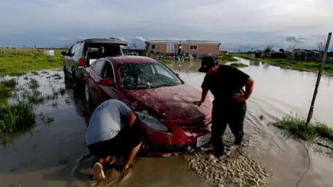 Getty Images People try to move a car in floodwater