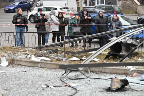 AFP People react standing behind the cordoned off area around the remains of a shell in Kyiv on 24 February 2022