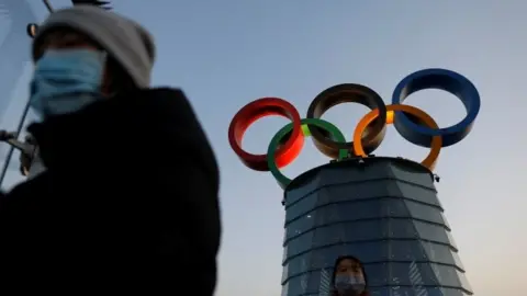 Reuters People wearing masks walk by the Olympic Tower in Beijing