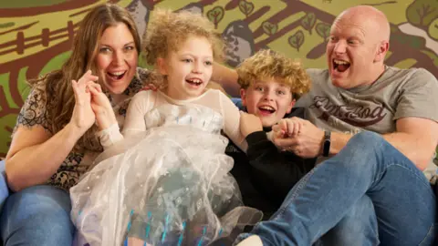 Julia's House The family site together smiling - two children between two adults.