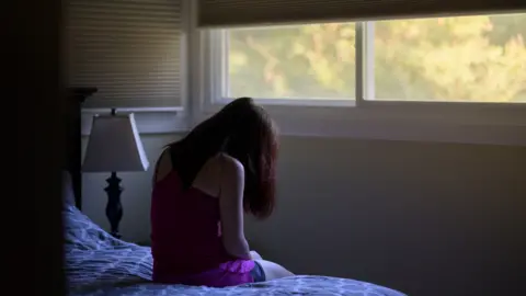 Getty Images File image of a woman sitting in a room with her head in her hands