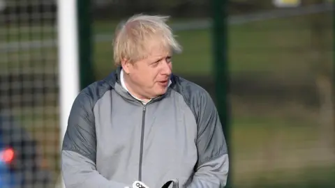 Getty Images British Prime Minister Boris Johnson puts on goalkeeping gloves before a girls" soccer match during an election campaign event on December 7, 2019 in Cheadle Hulme, United Kingdom