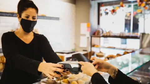 Getty Images Contactless payment in bakery with staff member in a mask