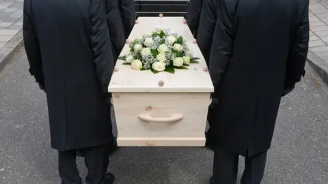 Getty Images Pallbearers carry an MDF casket adorned with flowers at a funeral ceremony