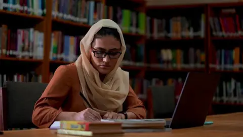 Wahida writing in a library