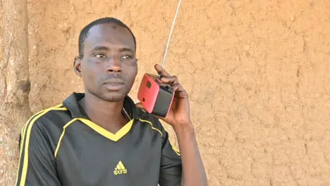 Nduka Orjinmo/ BBC A man holding a radio to his ear