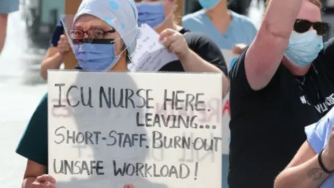 Getty Images A nurse holding a sign that says colleagues are short-staffed and burnt out at 2021 rally in Toronto, Canada.